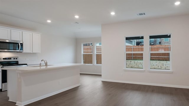 kitchen with dark wood-type flooring, a kitchen island with sink, a sink, appliances with stainless steel finishes, and baseboards