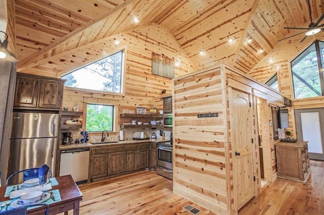 kitchen featuring wooden walls, sink, stainless steel appliances, and high vaulted ceiling