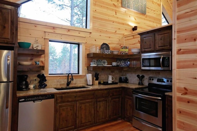 kitchen with decorative backsplash, stainless steel appliances, wooden walls, and sink