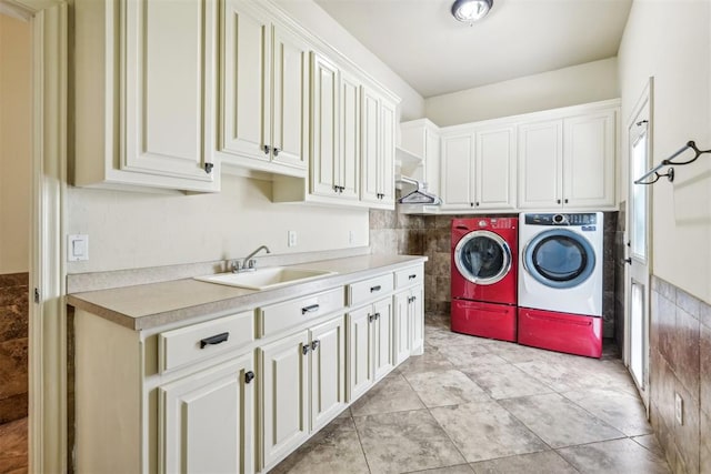 washroom featuring washing machine and clothes dryer, sink, light tile patterned flooring, and cabinets