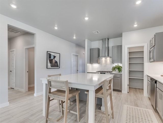 kitchen featuring gray cabinets, wall chimney range hood, stainless steel appliances, and light hardwood / wood-style flooring