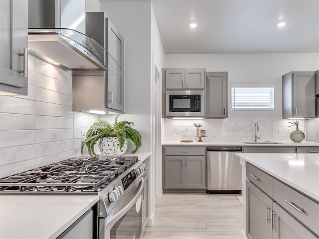 kitchen with appliances with stainless steel finishes, tasteful backsplash, gray cabinetry, wall chimney exhaust hood, and sink