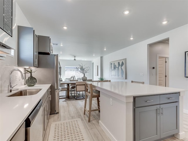 kitchen featuring a center island, sink, stainless steel dishwasher, gray cabinets, and light wood-type flooring