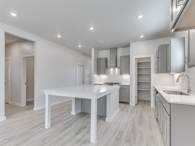 kitchen with gray cabinetry, sink, wall chimney exhaust hood, tasteful backsplash, and a kitchen island