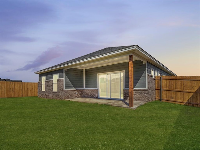 back house at dusk featuring a yard and a patio area