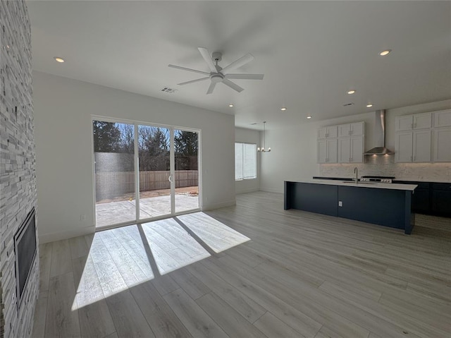 unfurnished living room featuring light wood-type flooring, a fireplace, sink, and ceiling fan with notable chandelier