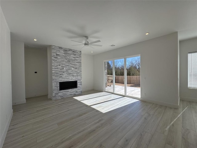 unfurnished living room with ceiling fan, light hardwood / wood-style flooring, a stone fireplace, and a healthy amount of sunlight