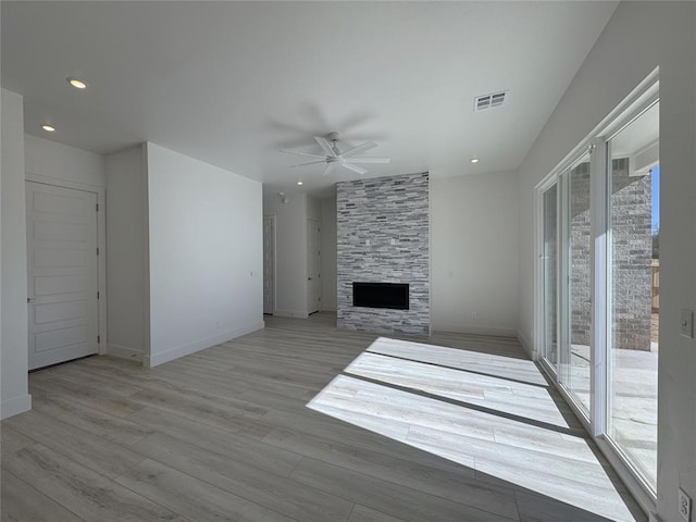 unfurnished living room with ceiling fan, a wealth of natural light, a stone fireplace, and light hardwood / wood-style flooring