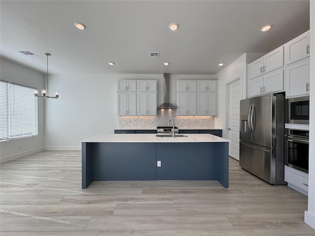 kitchen featuring appliances with stainless steel finishes, decorative backsplash, decorative light fixtures, wall chimney exhaust hood, and sink