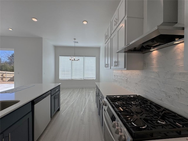 kitchen featuring appliances with stainless steel finishes, backsplash, a notable chandelier, decorative light fixtures, and wall chimney range hood