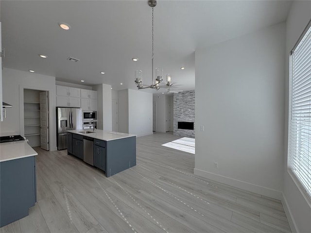 kitchen with decorative light fixtures, stainless steel appliances, a fireplace, sink, and a center island with sink