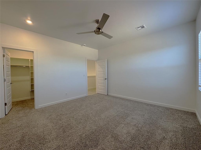 unfurnished bedroom with ceiling fan, a closet, a spacious closet, and carpet floors