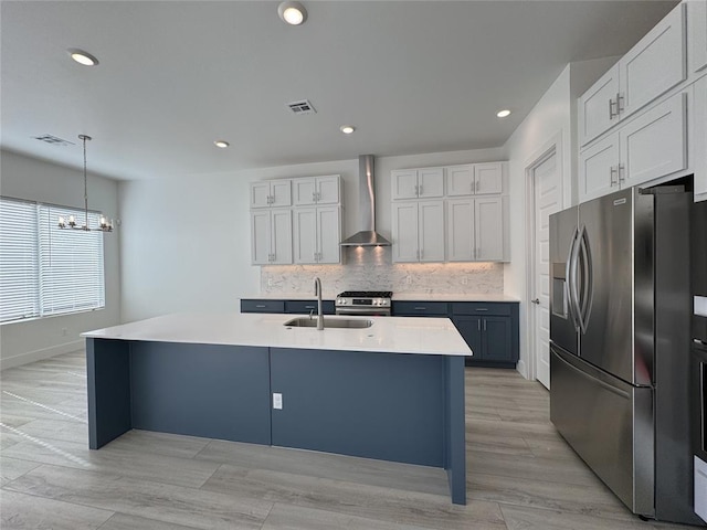 kitchen with a center island with sink, wall chimney exhaust hood, stainless steel appliances, and pendant lighting