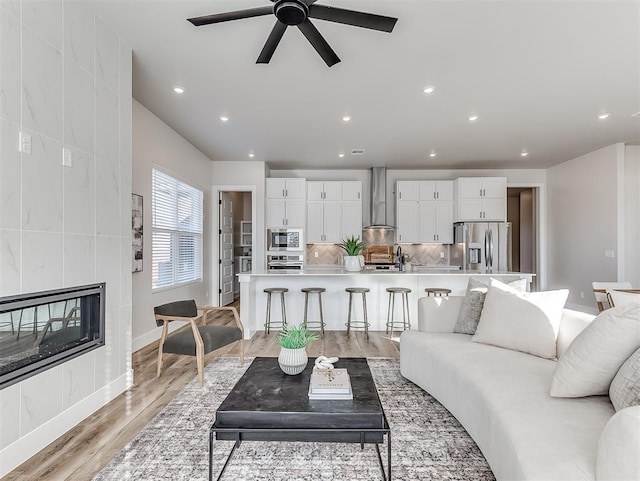 living room featuring ceiling fan, light hardwood / wood-style floors, a tile fireplace, and sink