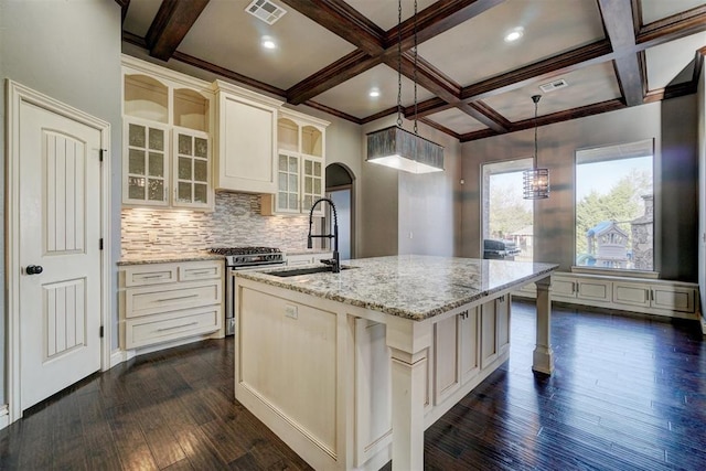 kitchen with stainless steel gas range oven, an island with sink, dark hardwood / wood-style flooring, hanging light fixtures, and sink