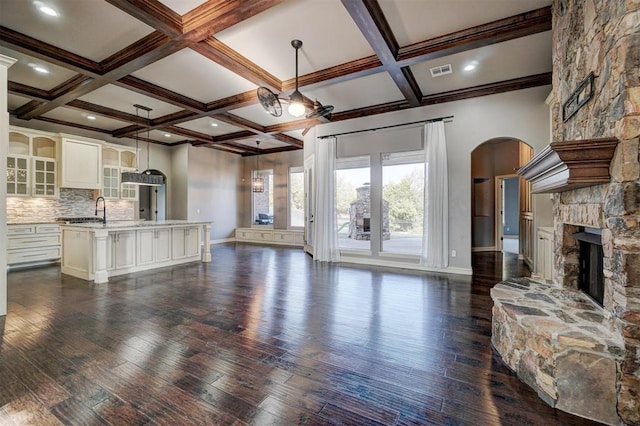 living room with beam ceiling, a stone fireplace, and coffered ceiling