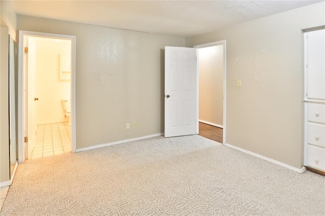 unfurnished bedroom featuring a textured ceiling, ensuite bathroom, and light carpet