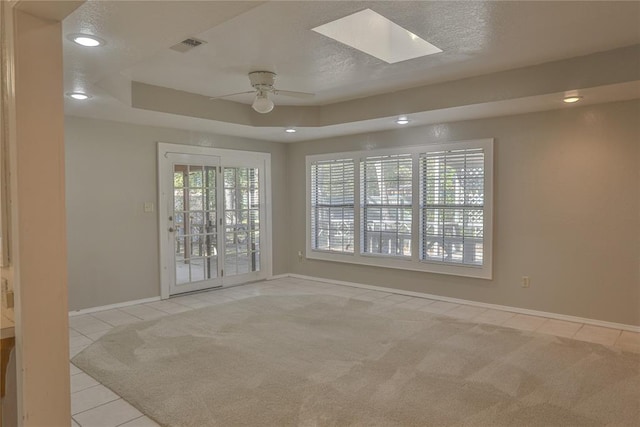 carpeted empty room with a textured ceiling, a skylight, ceiling fan, and a healthy amount of sunlight