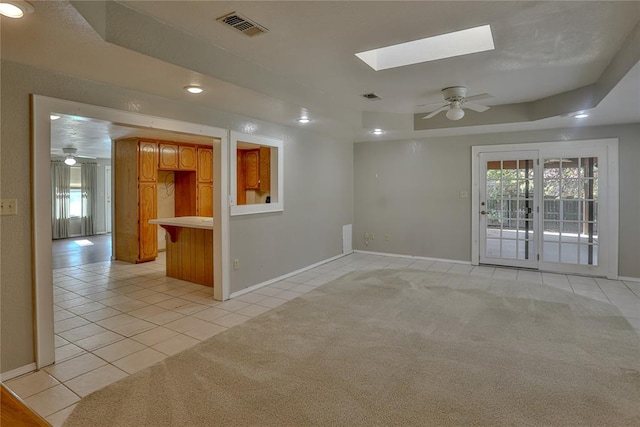 carpeted empty room with a raised ceiling, a skylight, and ceiling fan