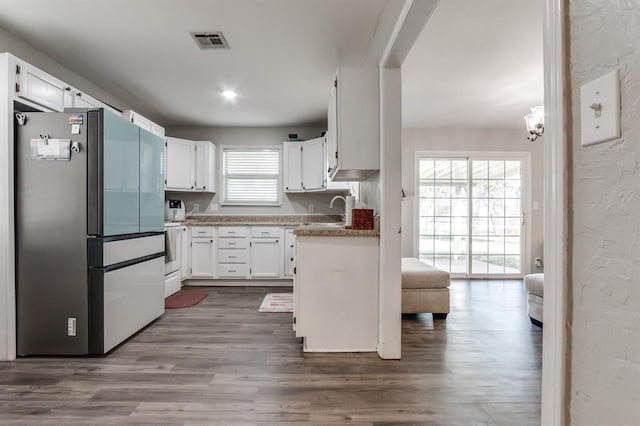 kitchen with white cabinets, plenty of natural light, hardwood / wood-style floors, and stainless steel refrigerator