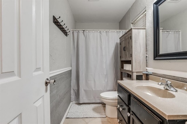 bathroom with toilet, vanity, tile patterned floors, and tile walls