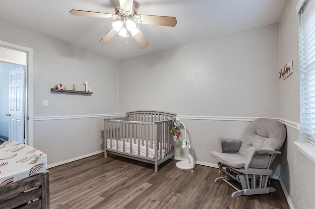 bedroom featuring ceiling fan, dark hardwood / wood-style flooring, and a nursery area