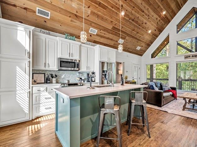 kitchen featuring white cabinets, appliances with stainless steel finishes, decorative light fixtures, and a kitchen island with sink