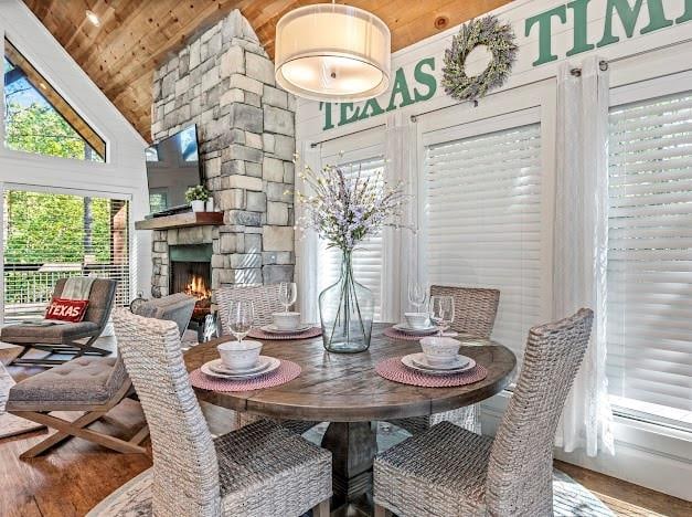 dining area with hardwood / wood-style floors, a stone fireplace, wooden ceiling, and high vaulted ceiling