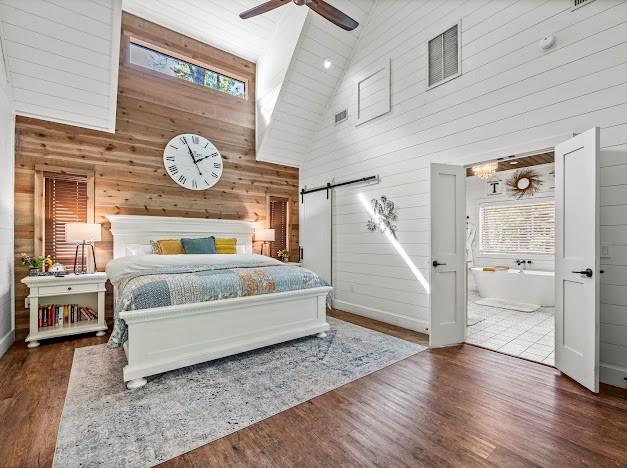 bedroom with ceiling fan, wooden walls, high vaulted ceiling, and dark hardwood / wood-style floors