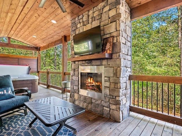 wooden deck featuring an outdoor stone fireplace, ceiling fan, and a hot tub