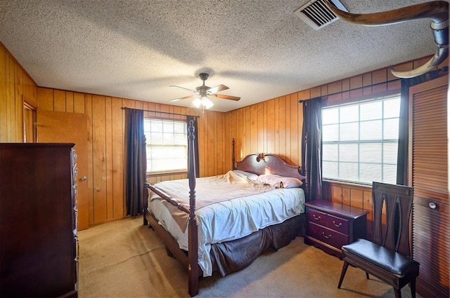 carpeted bedroom with ceiling fan, wooden walls, and multiple windows