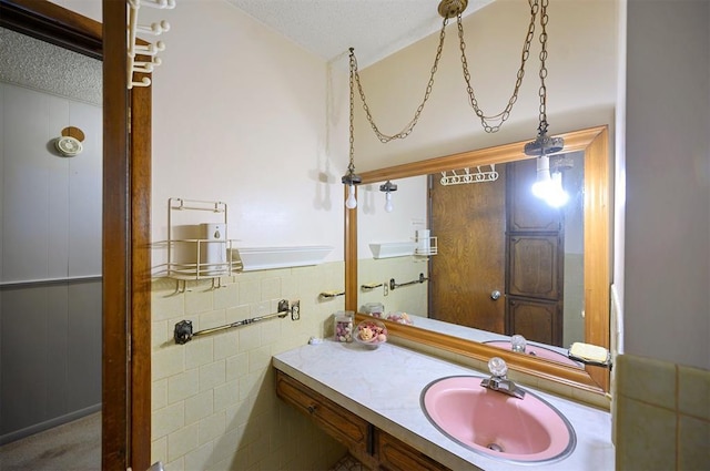 bathroom featuring a textured ceiling, vanity, and tile walls