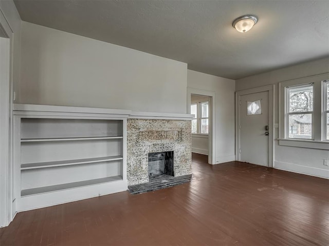 unfurnished living room featuring a stone fireplace and dark wood-type flooring