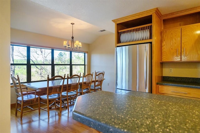 kitchen with dark wood-type flooring, a notable chandelier, stainless steel refrigerator, hanging light fixtures, and lofted ceiling