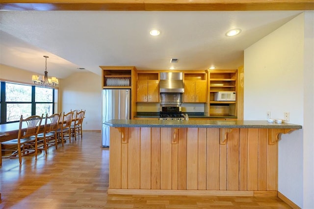 kitchen featuring decorative light fixtures, light hardwood / wood-style flooring, wall chimney exhaust hood, appliances with stainless steel finishes, and a notable chandelier