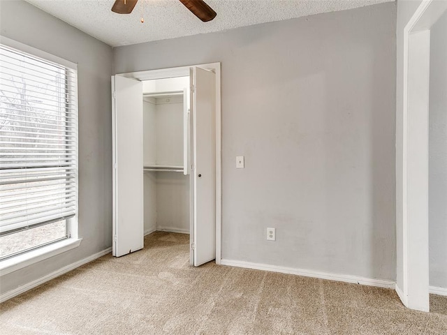 unfurnished bedroom featuring a textured ceiling, light colored carpet, multiple windows, and ceiling fan