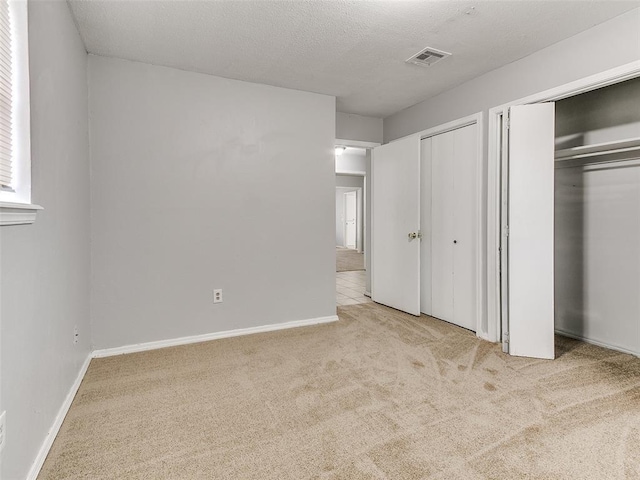 unfurnished bedroom featuring light colored carpet, a textured ceiling, and multiple closets