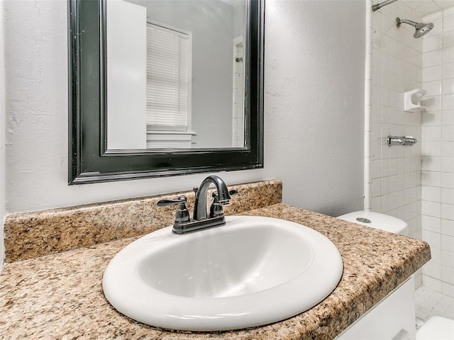 bathroom with toilet, vanity, and tiled shower