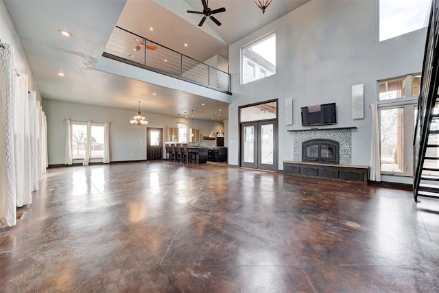 unfurnished living room with ceiling fan with notable chandelier, a fireplace, and a high ceiling