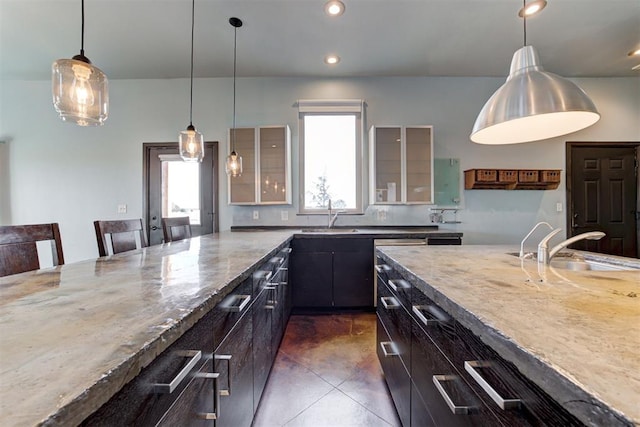 kitchen with sink, light stone counters, a kitchen bar, and hanging light fixtures