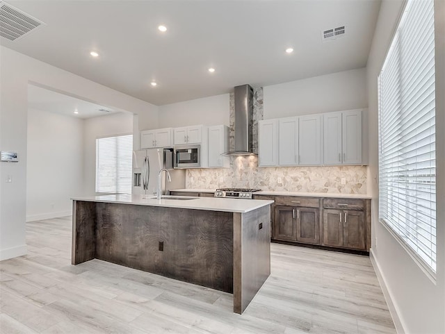 kitchen featuring a spacious island, wall chimney exhaust hood, sink, stainless steel fridge, and built in microwave