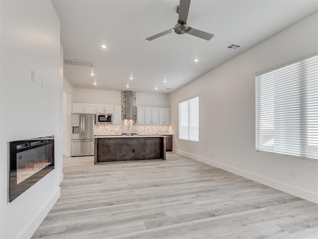 kitchen with appliances with stainless steel finishes, decorative backsplash, wall chimney range hood, a kitchen island, and white cabinets