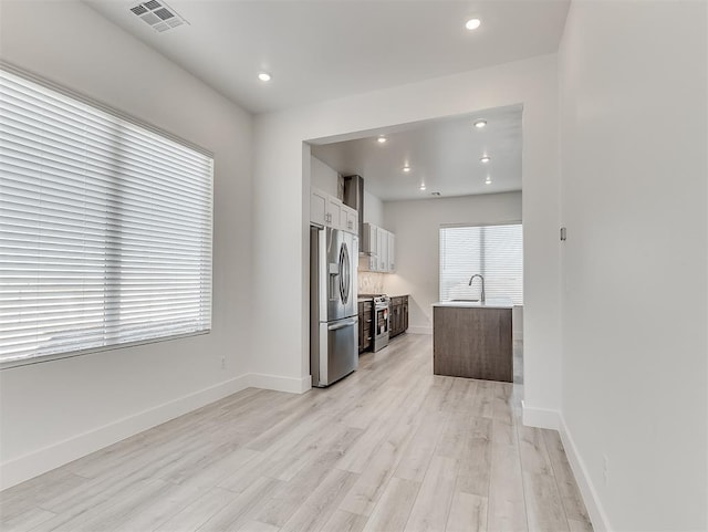 kitchen with sink, white cabinetry, a kitchen island with sink, light hardwood / wood-style floors, and stainless steel appliances