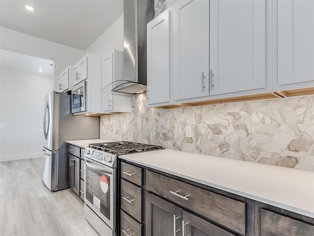 kitchen with light hardwood / wood-style flooring, appliances with stainless steel finishes, white cabinetry, tasteful backsplash, and wall chimney range hood