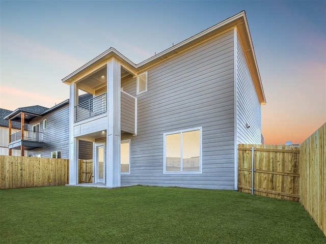 back house at dusk with a balcony and a lawn