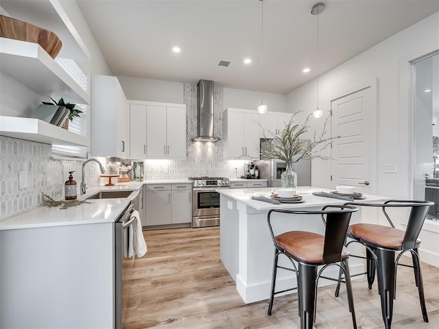 kitchen featuring appliances with stainless steel finishes, decorative light fixtures, wall chimney exhaust hood, white cabinets, and sink