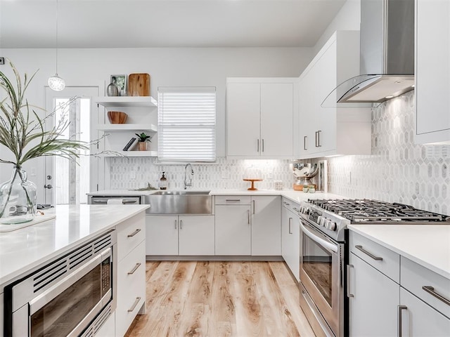 kitchen with pendant lighting, sink, white cabinetry, stainless steel appliances, and wall chimney exhaust hood