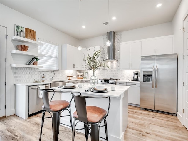 kitchen featuring a center island, decorative light fixtures, wall chimney range hood, stainless steel appliances, and a kitchen breakfast bar