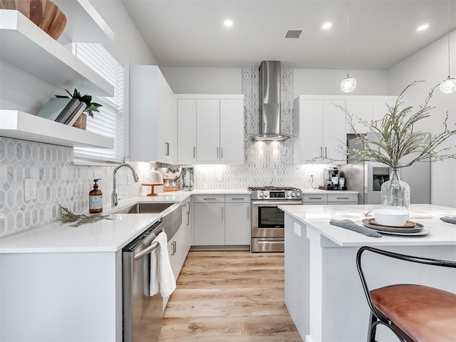 kitchen featuring appliances with stainless steel finishes, pendant lighting, wall chimney exhaust hood, white cabinets, and sink