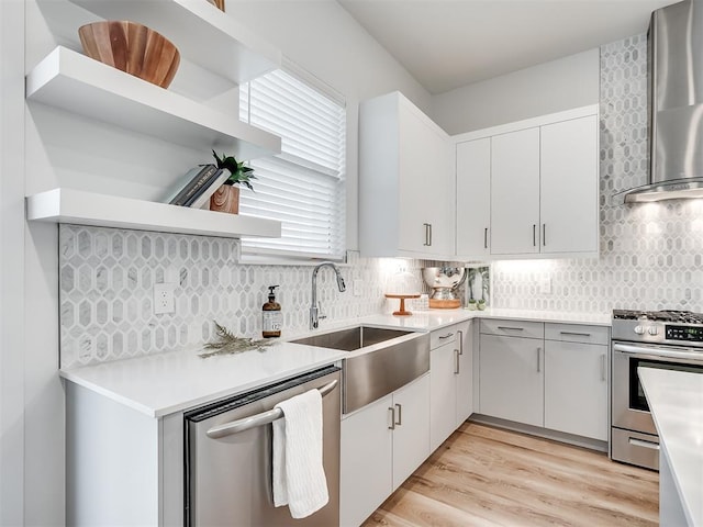 kitchen featuring white cabinets, appliances with stainless steel finishes, wall chimney range hood, sink, and backsplash